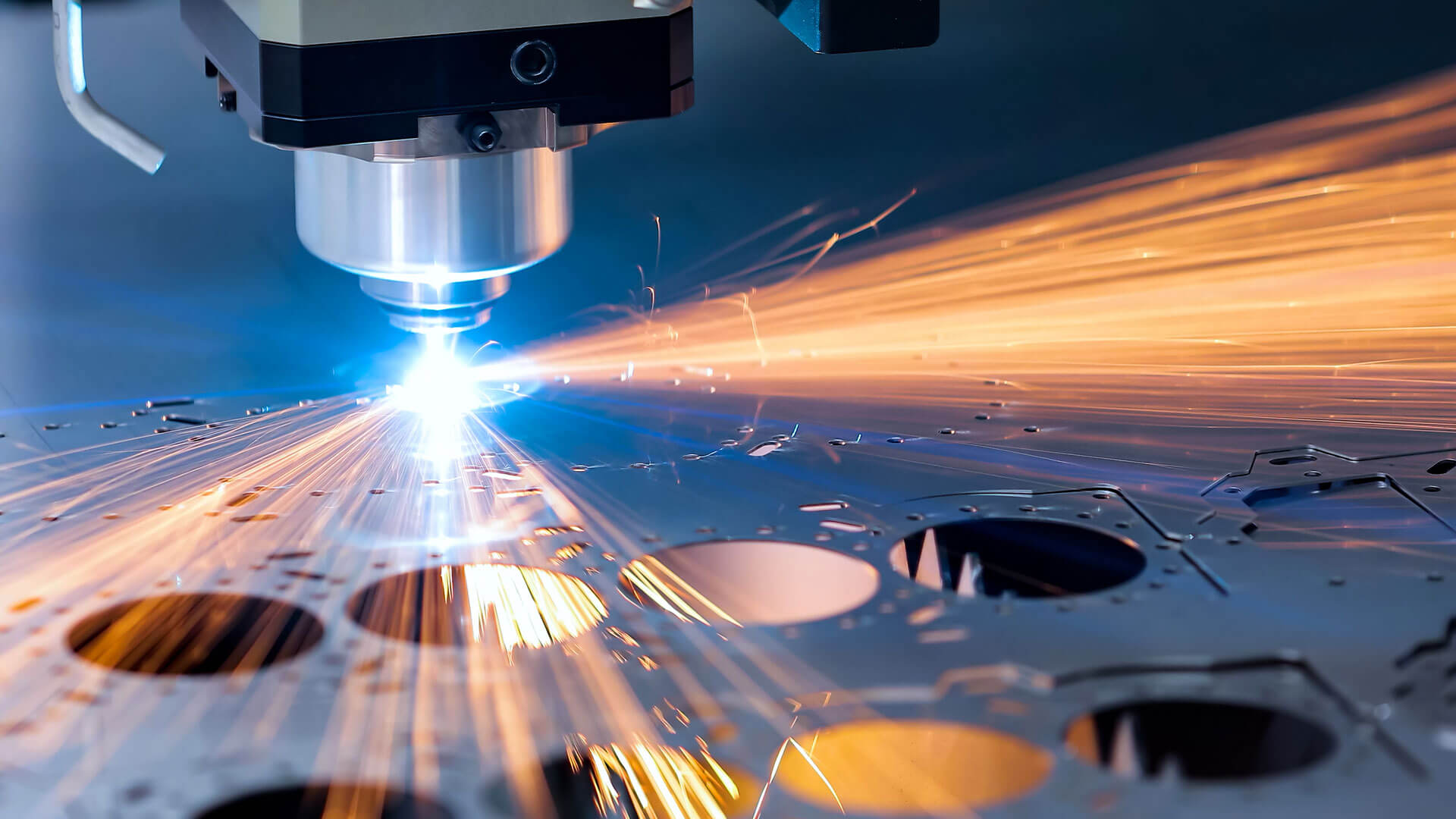 A laser cutter firing a blue beam into a solid block of metal, sparks are flying from the point of impact
